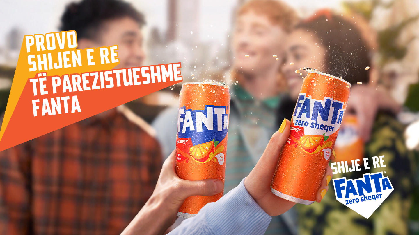 Dy kanaçe Fanta portokalli, njëra zero sheqer, shpërthejnë me flluska, mbajtur nga duar para njerëzish. "Provo shijen e re!"
