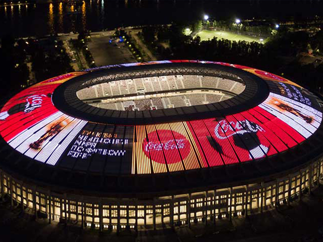 Fotografija pokazuje nogometni stadio kako svijetli u mraku prekriven Coca-Cola reklamama