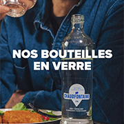 Une personne boit un verre d’eau dans un restaurant, avec une bouteille en verre Chaudfontaine posée sur la table. Texte sur l’image : « NOS BOUTEILLES EN VERRE ».