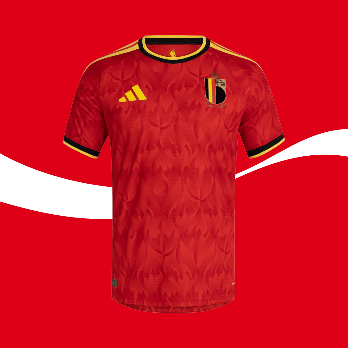 Een rood Belgisch voetbalshirt met subtiel vlammenpatroon, gele en zwarte accenten, het nationale embleem op de borst en een sportlogo, afgebeeld tegen een rode achtergrond.