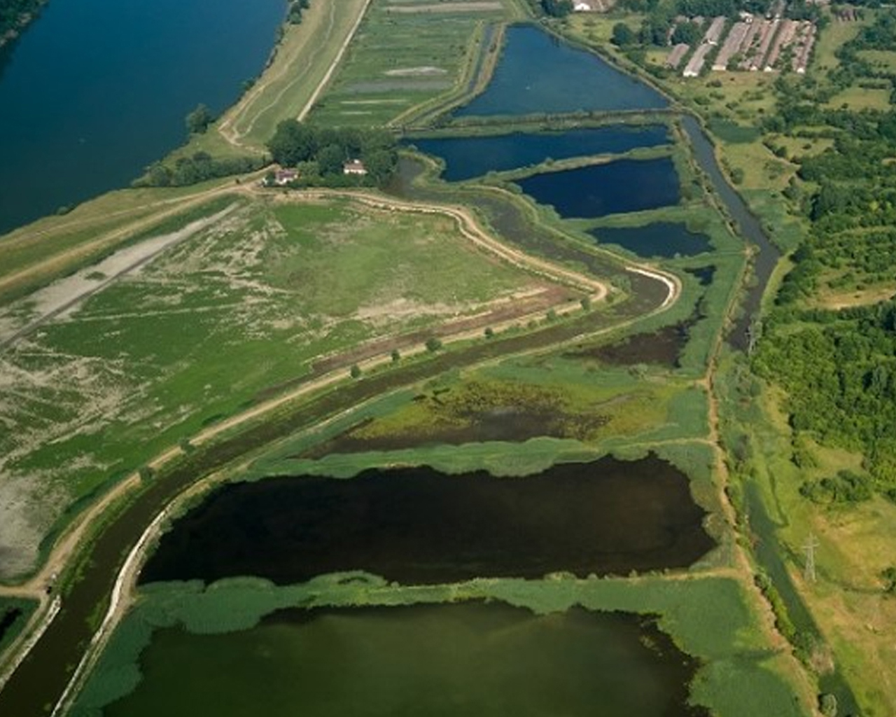 Luchtfoto van een landschap met meerdere waterbekkens en vijvers, omringd door groene begroeiing en enkele gebouwen in de verte.
