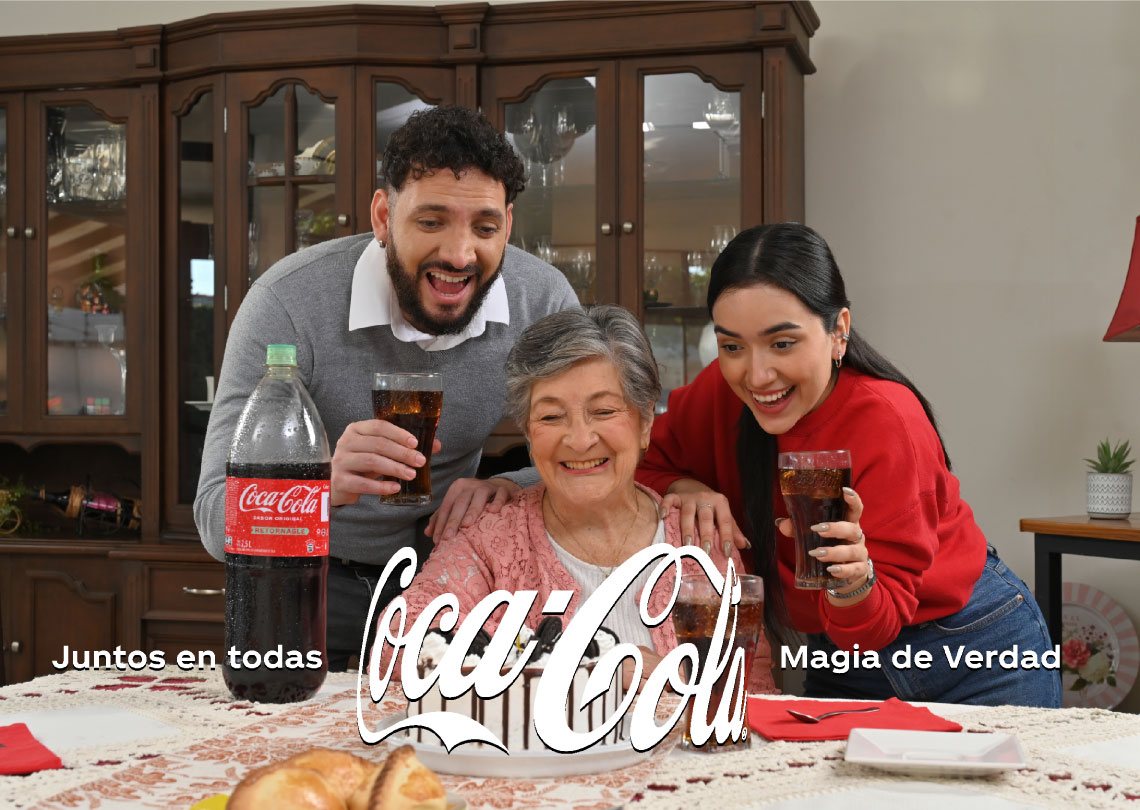Una familia sonríe mientras brindan con vasos de Coca-Cola Sabor Original en una reunión hogareña.