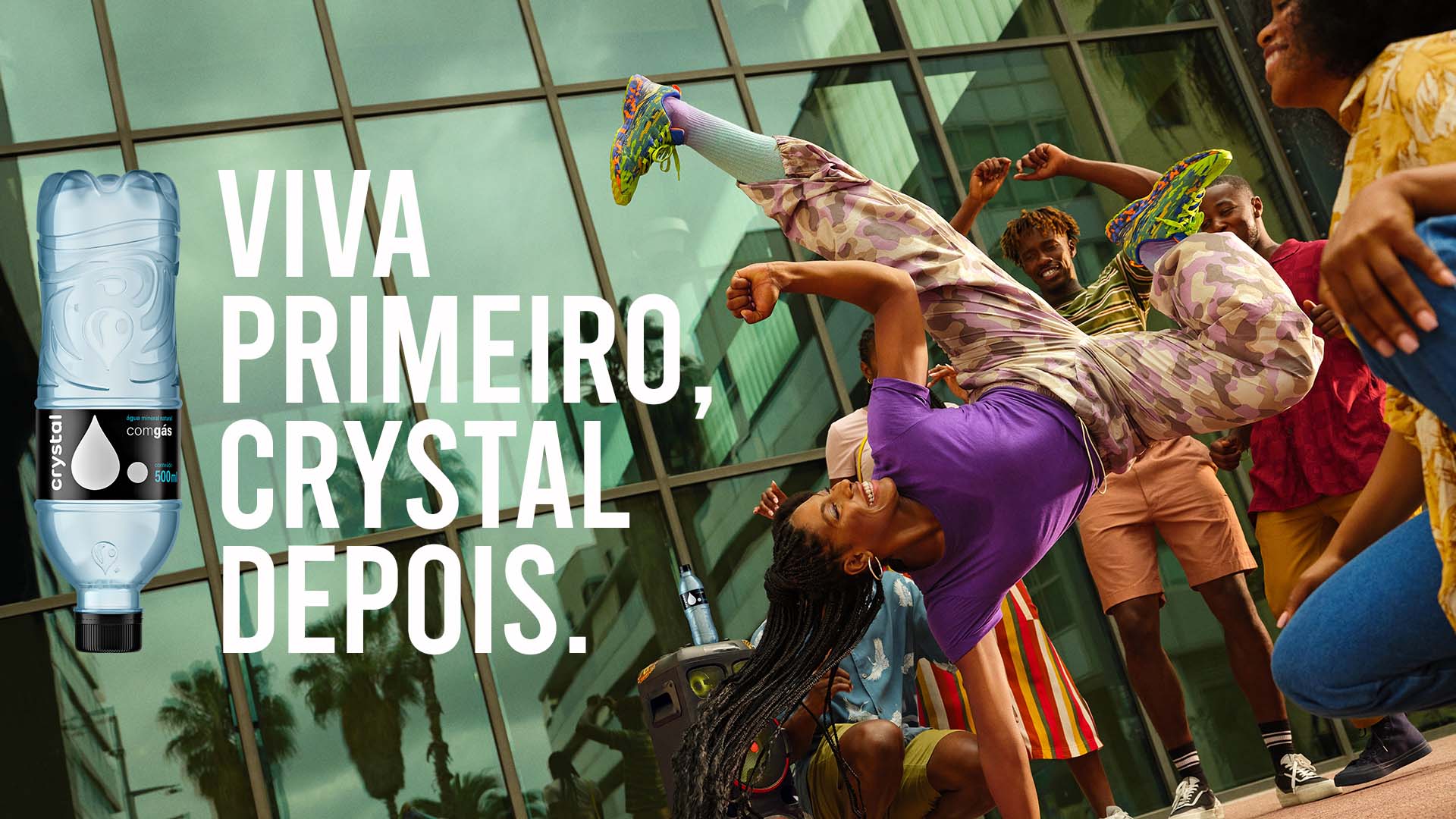 Grupo de amigos se divertindo e dançando, com água Crystal para se hidratar. Com o texto "Viva primerio, Crystal depois"  em cima, e uma garrafa do agua Crystal com gas.