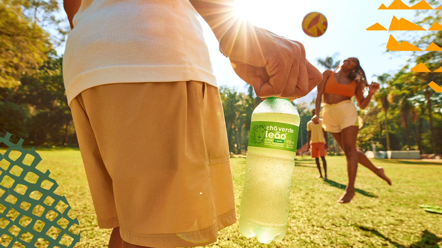 pessoas em um parque brincando com uma bola e uma delas segurando uma garrafa de Chás Verde Leão