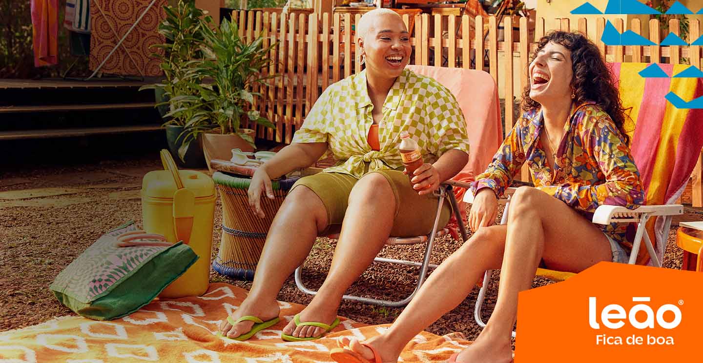 duas mulheres sentadas em uma espreguiçadeira cada uma, rindo e bebendo um Chas Leão