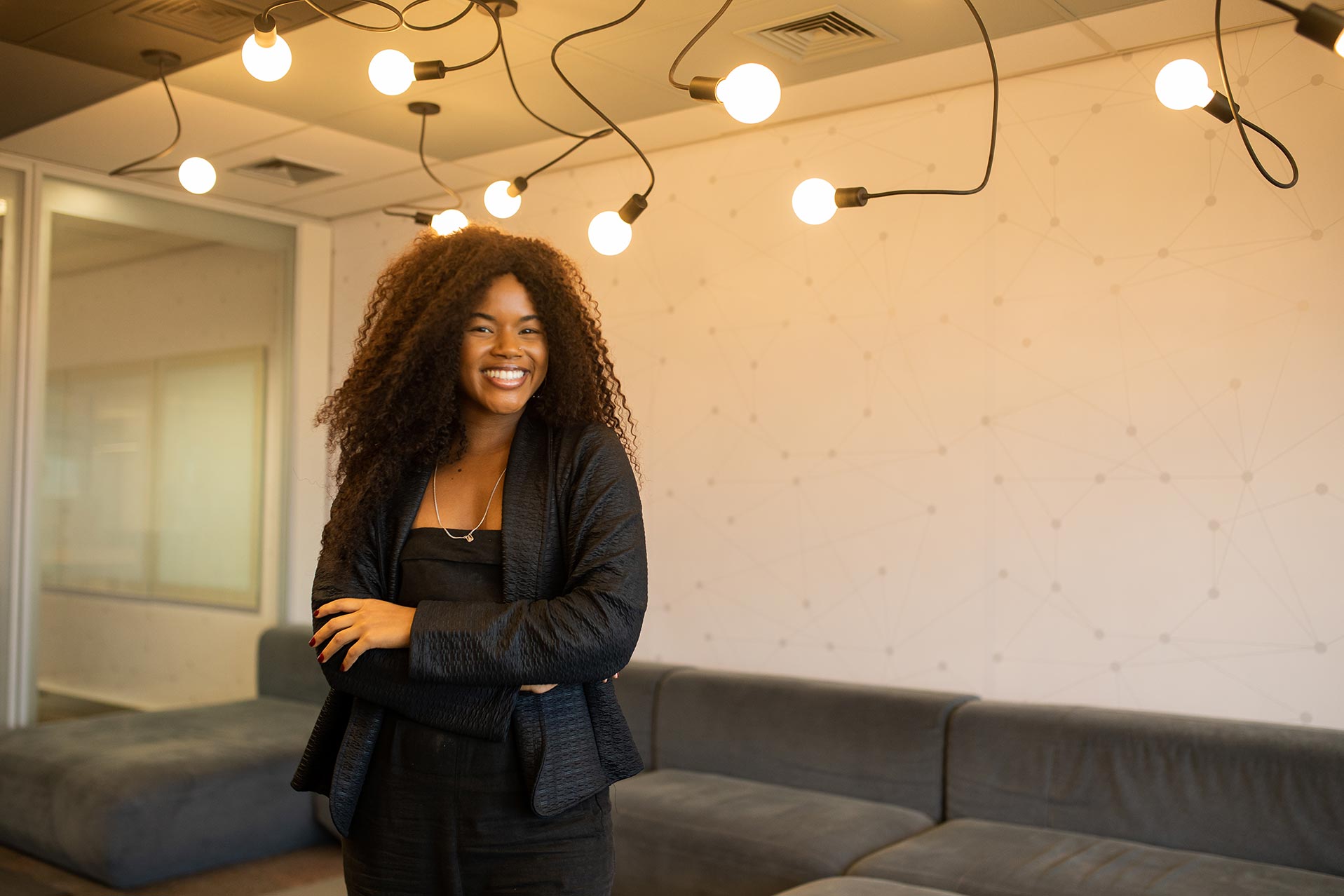 Jovem com cabelos cacheados e roupas pretas posa e sorri.