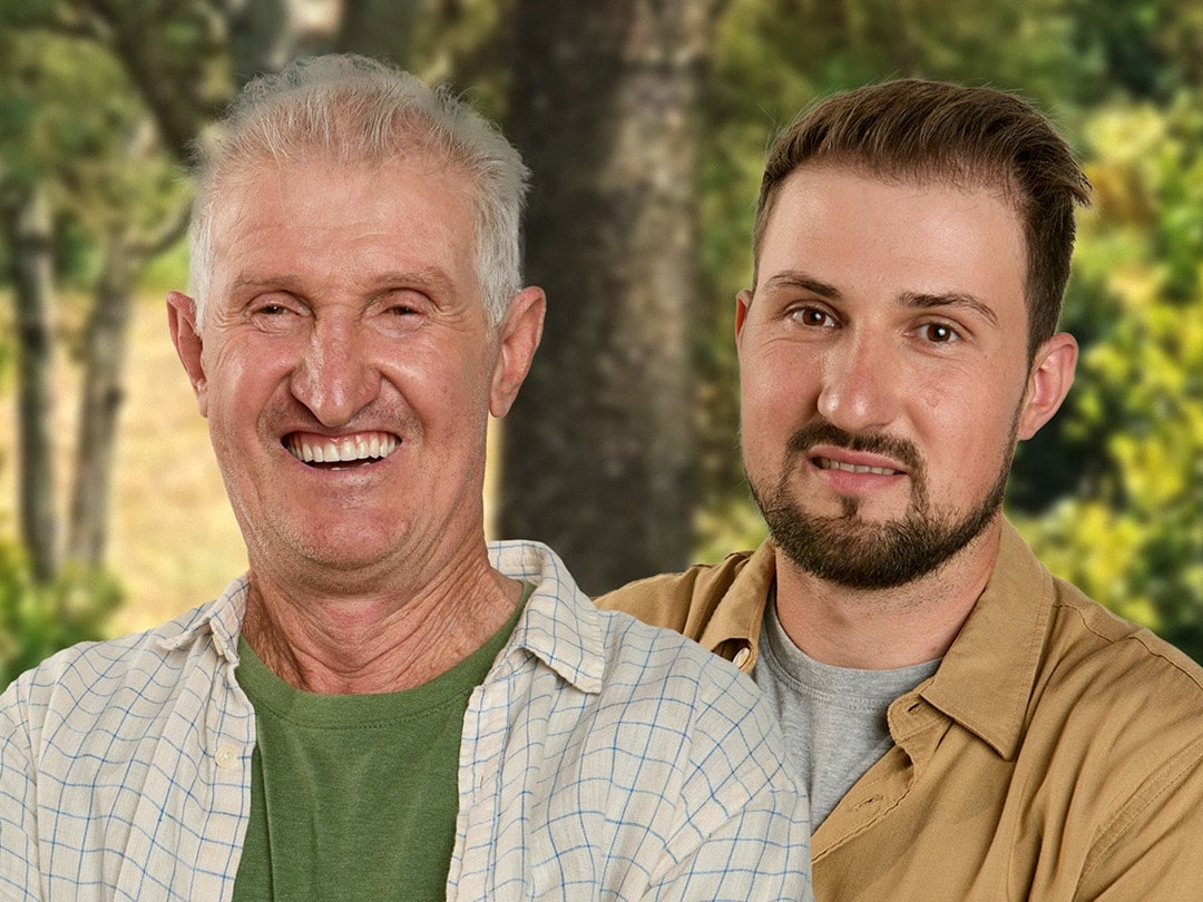 Um homem idoso sorrindo ao lado de um homem mais jovem em um ambiente rural.