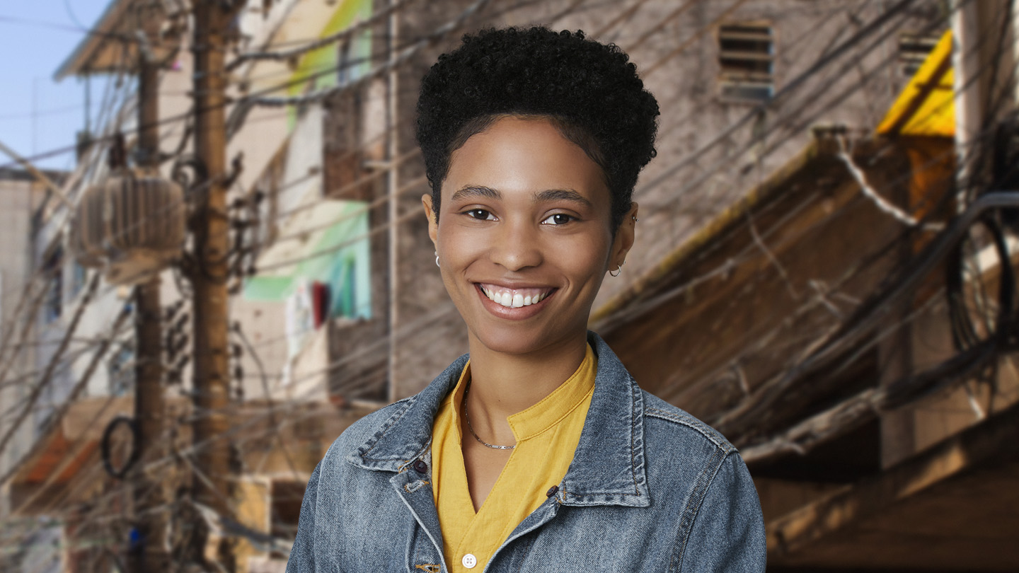 Mulher sorridente com cabelo curto e jaqueta jeans, em frente a uma paisagem urbana com fiação elétrica.