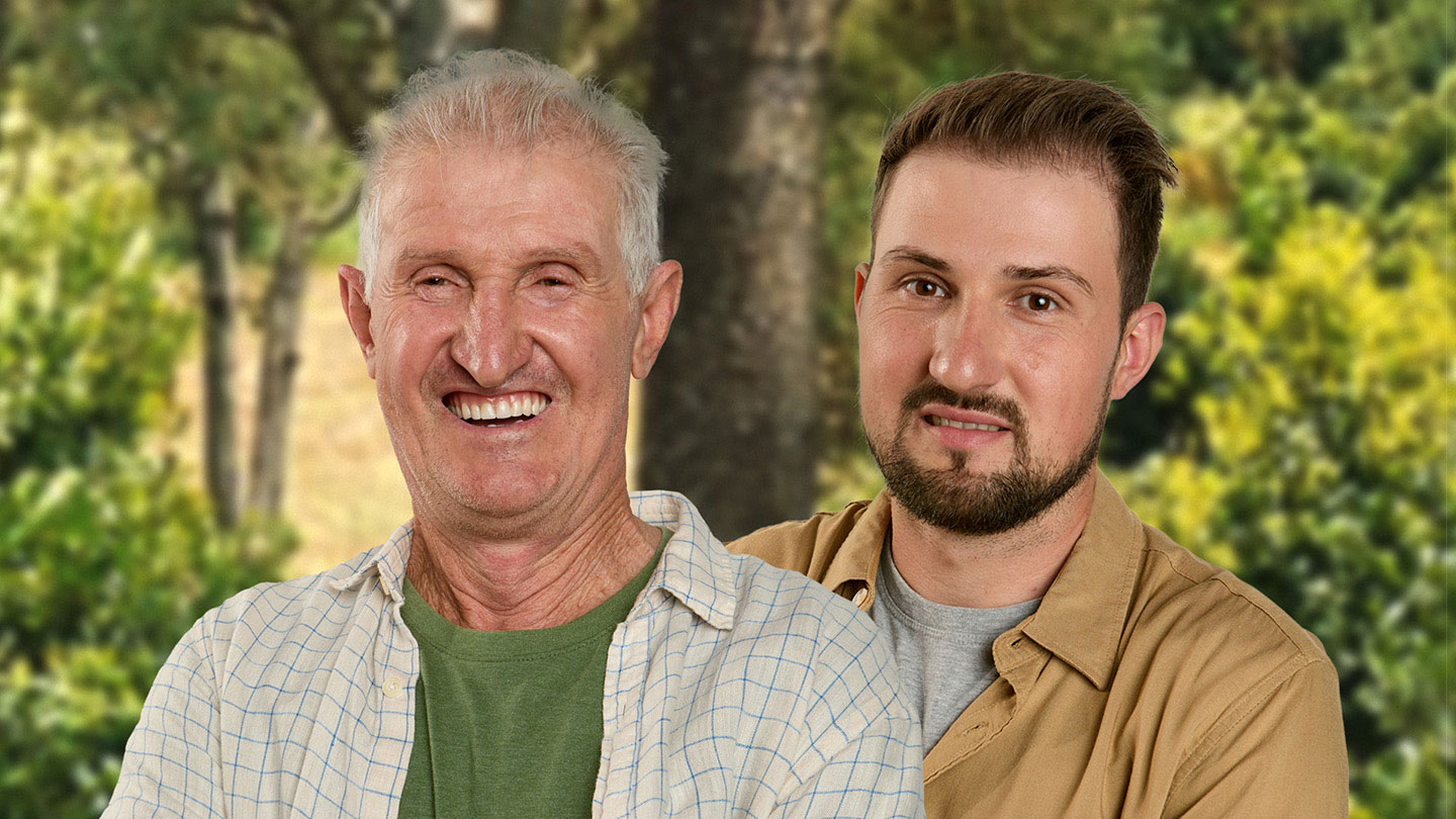 Um homem idoso sorrindo ao lado de um homem mais jovem em um ambiente rural.