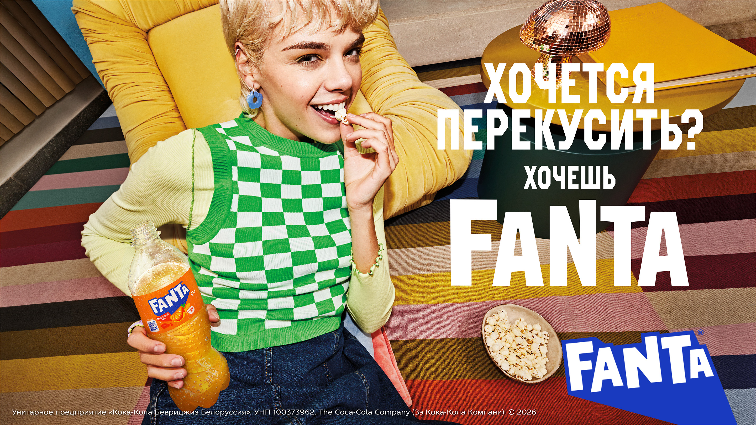 Чалавек адпачывае на канапе з бутэлькай Fanta і папкорнам, рэкламны банер напою.