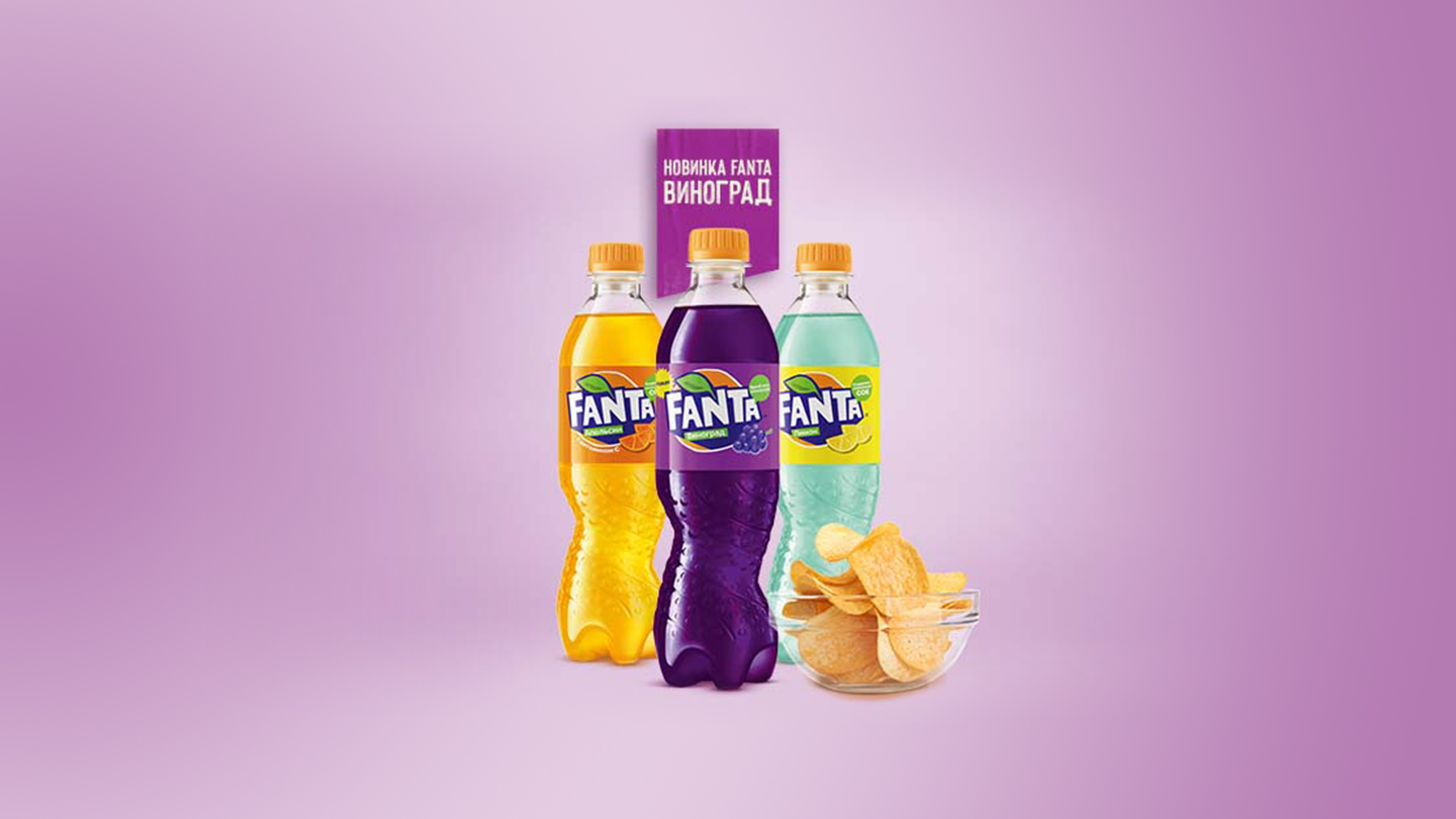 Тры бутэлькі Fanta розных смакаў і міска з чыпсамі на ружовым фоне