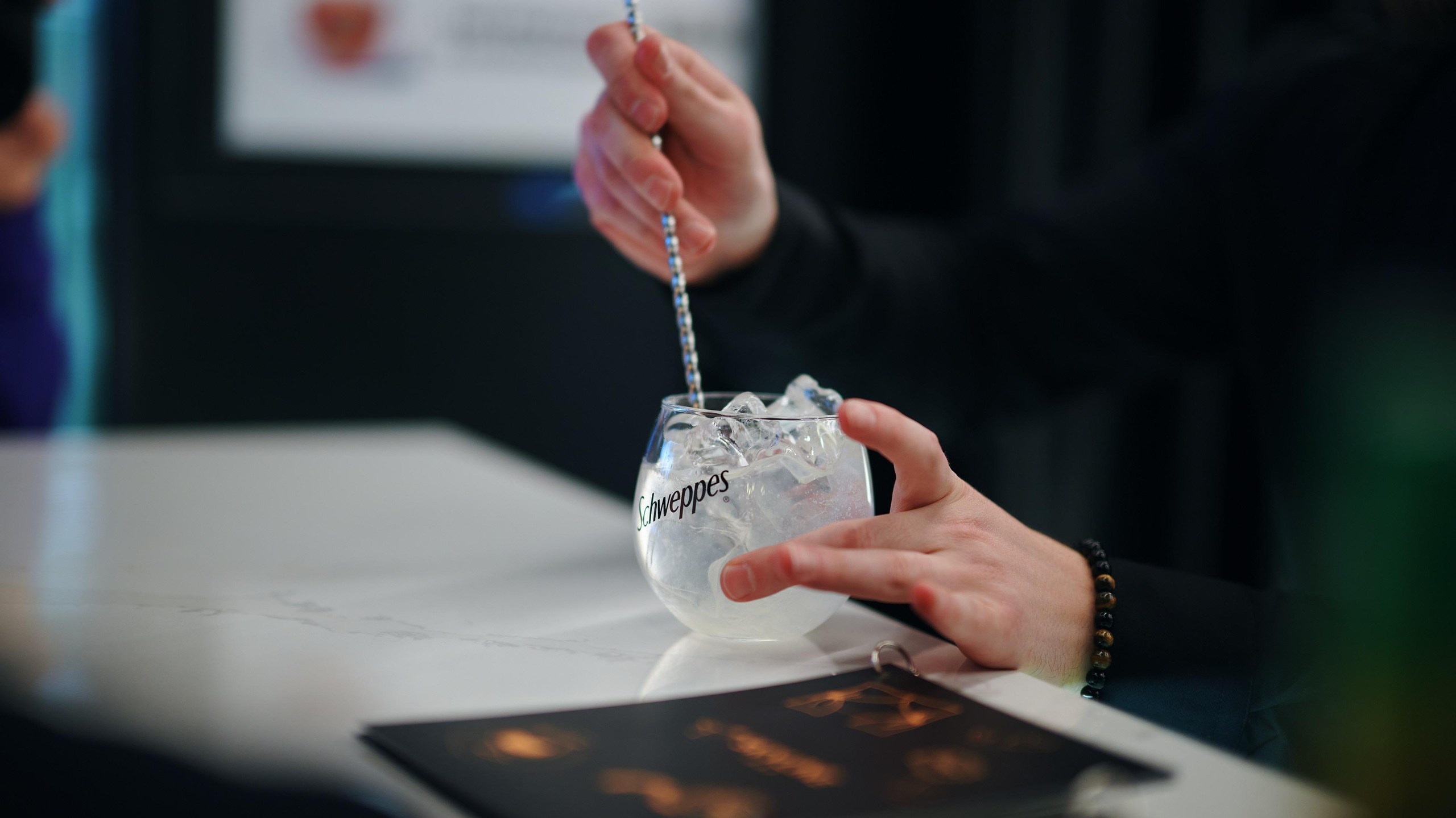 Рука змешвае лёд і напой у шклянцы Schweppes трубачкай
