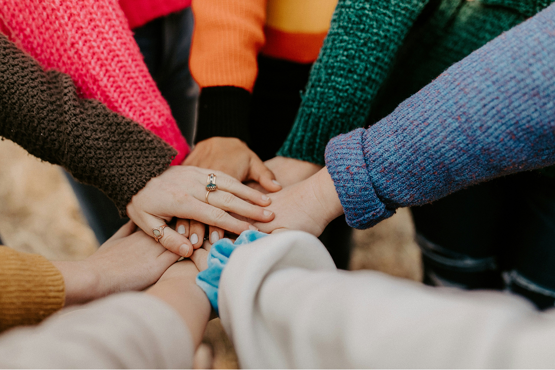 Several people standing in a circle all putting their hands together on top of one another