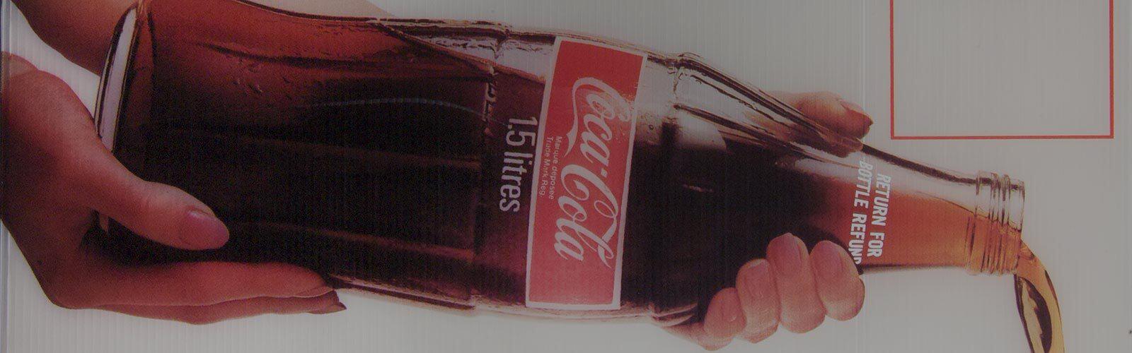 Zwei Hände halten eine Coca-Cola Flasche und kippen das Getränk aus