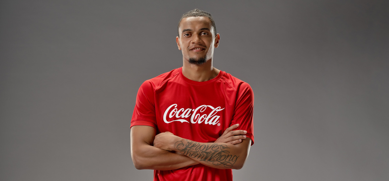 Footballeur suisse Manuel Akanji en t-shirt Coca-Cola sur fond gris.