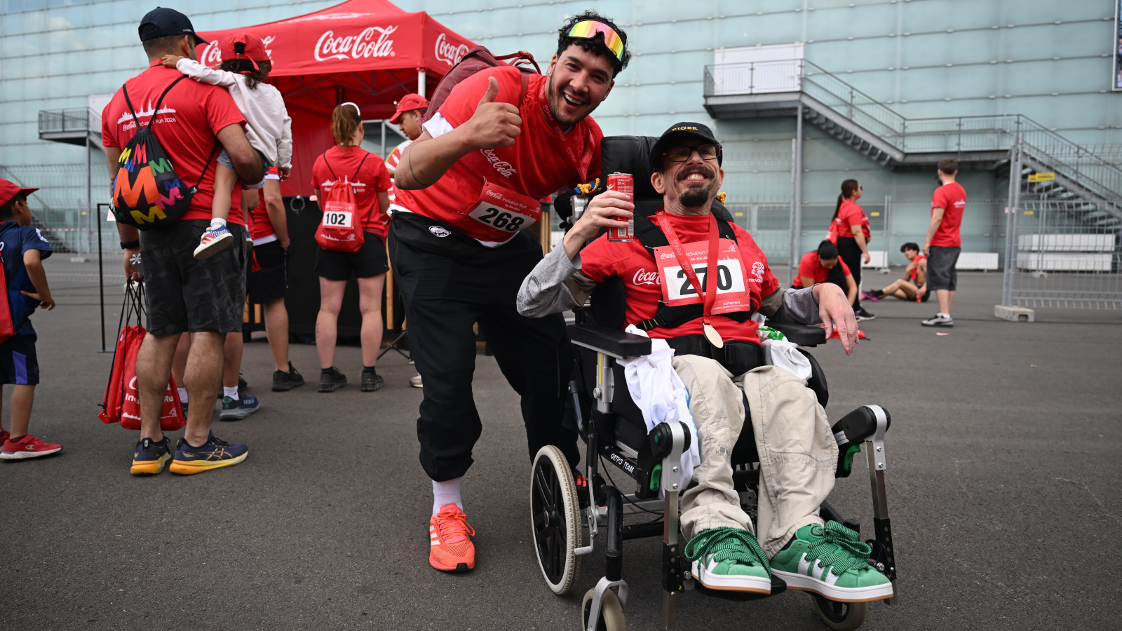 Deux jeunes hommes posent pour la caméra ; l’homme en fauteuil roulant tient un Coca-Cola.
