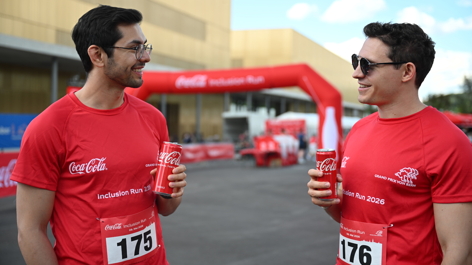 Deux jeunes hommes, une Coca-Cola à la main, se regardent.