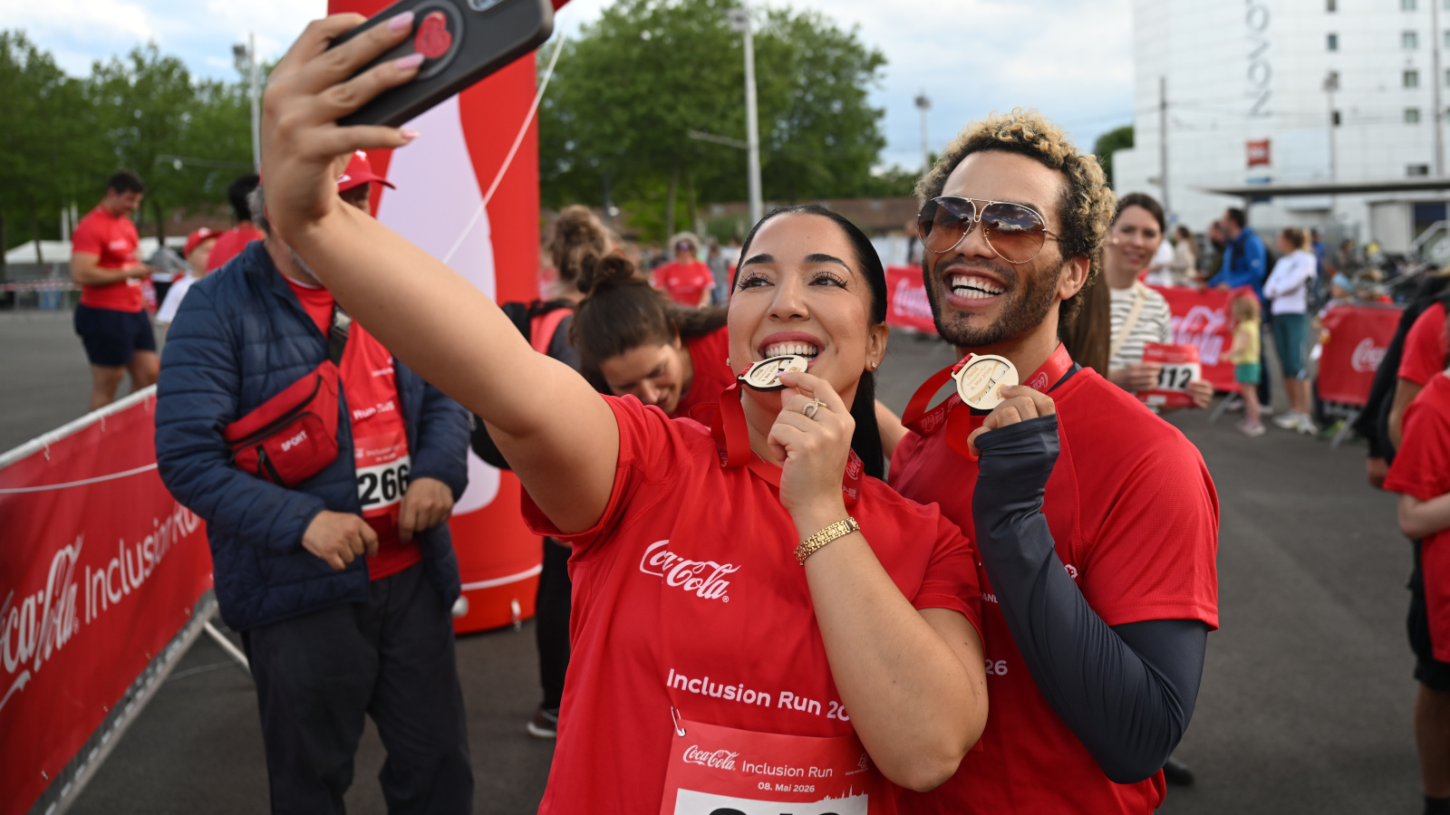 Une jeune femme et un jeune homme prennent un selfie, tandis que la jeune femme mord dans sa médaille.