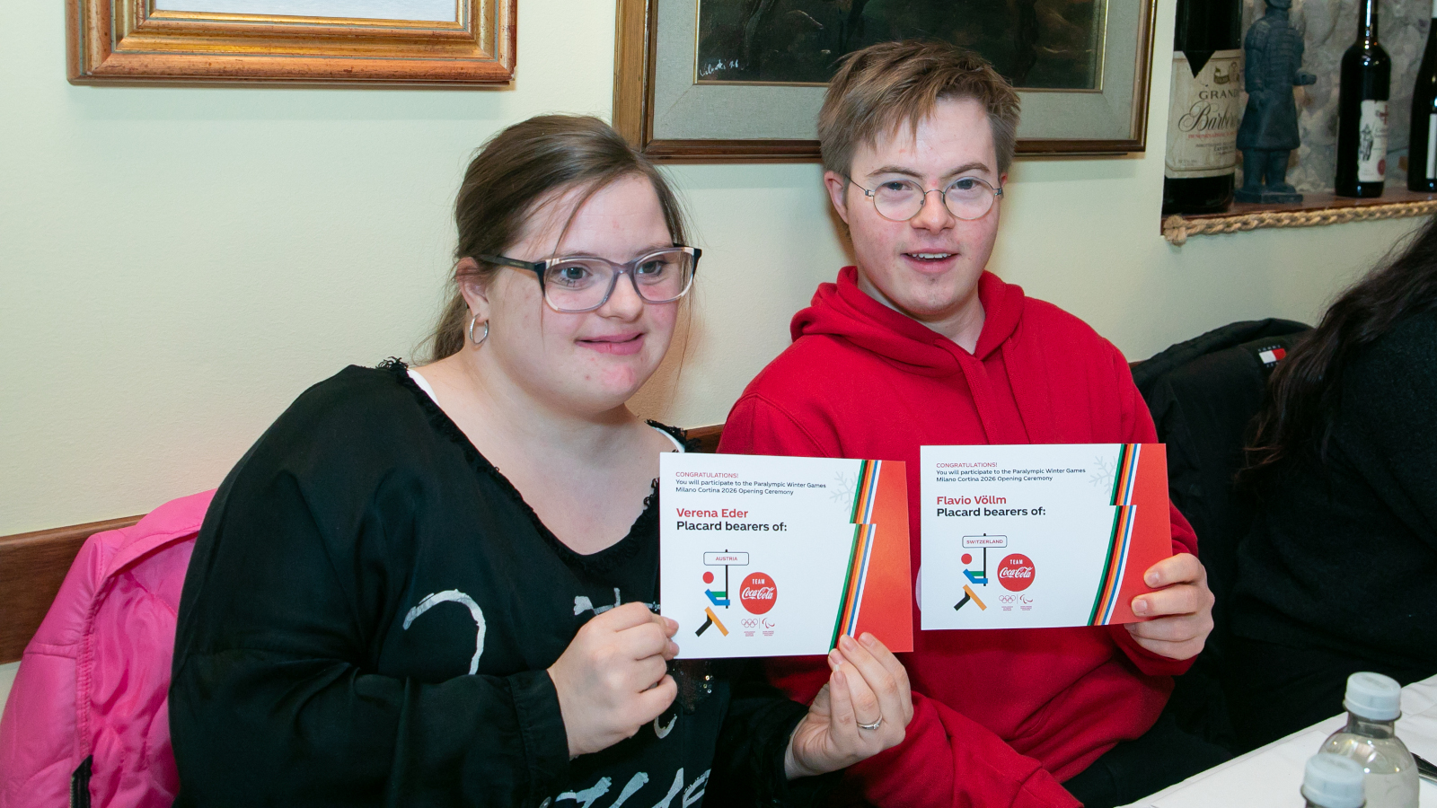 Verena, Special Olympics Sportlerin aus Österreich zusammen mit Flavio, Special Olympics Athlet aus der Schweiz mit der Einladung zum Schildträger in der Hand