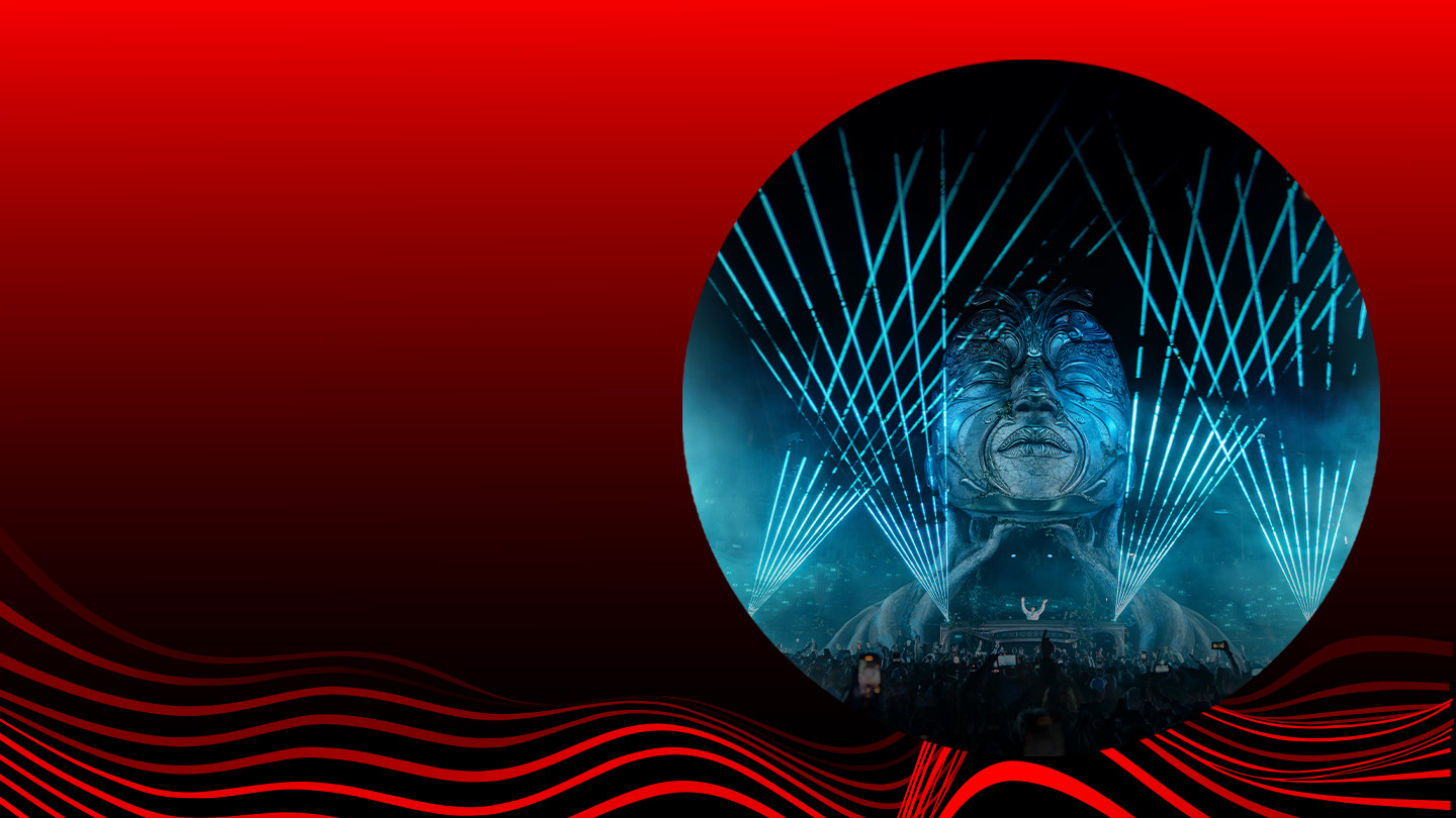 Fotografía de un escenario iluminado con luces láser azules y una gran escultura de rostro humano durante un concierto nocturno, enmarcado en un círculo sobre un fondo degradado de rojo a negro con ondas rojas estilizadas en la parte inferior.​