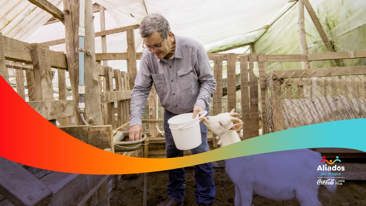 Hombre sonriente con un balde de color blanco en la mano y una cabra a su lado