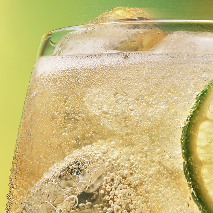 Klaas kuldse Schweppes mullijoogiga, milles on jääkuubikud ja laimiviil.