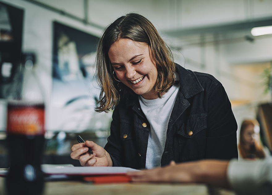 Isik kirjutamas laual asuvasse märkmikku, kõrval Coca-Cola pudel.