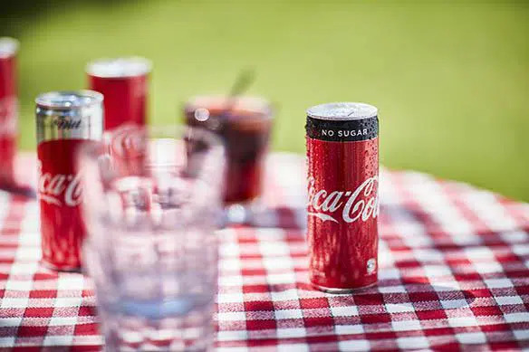 Coca‑Cola purgid ja klaasid punavalgel ruudulisel piknikulaual.