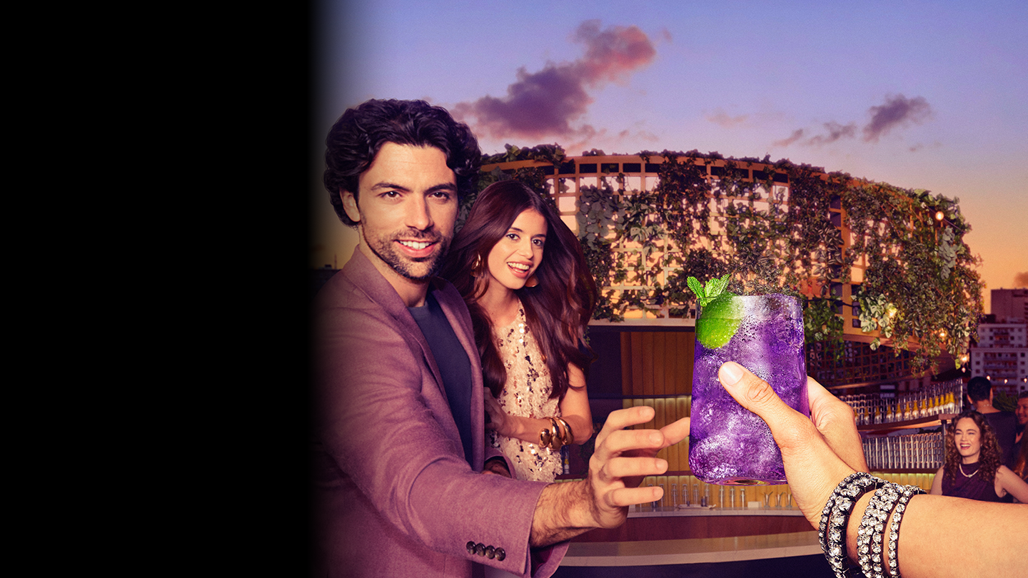 Muška osoba u ljubičastom sakou pruža ruku kako bi uzeo novi Schweppes Purple tonic u staklenoj čaši.