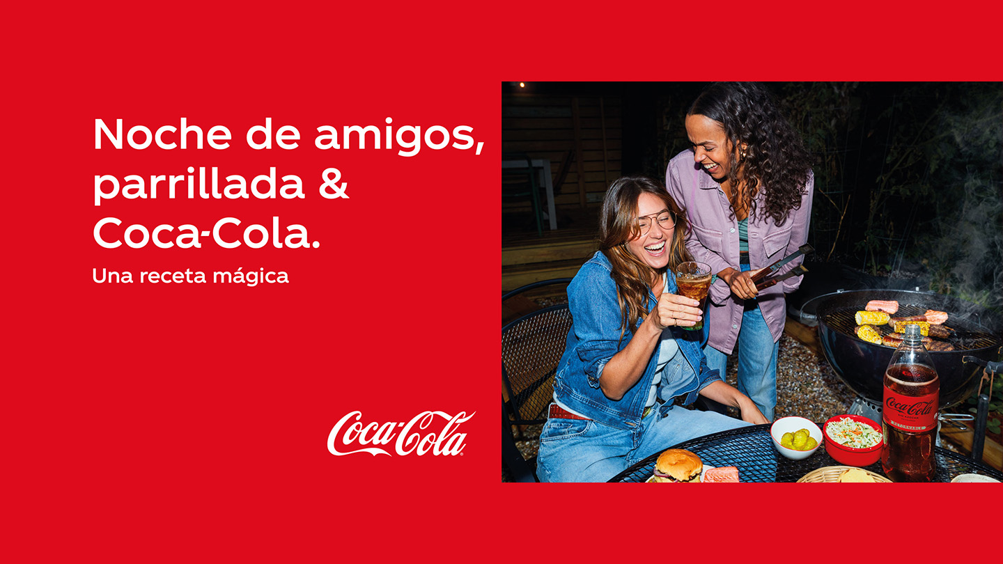 Dos amigas riendo cocinando una parrillada y bebiendo Coca-Cola sin azúcar junto al texto: noche de amigos, parrillada, y Coca-Cola. Una receta mágica.