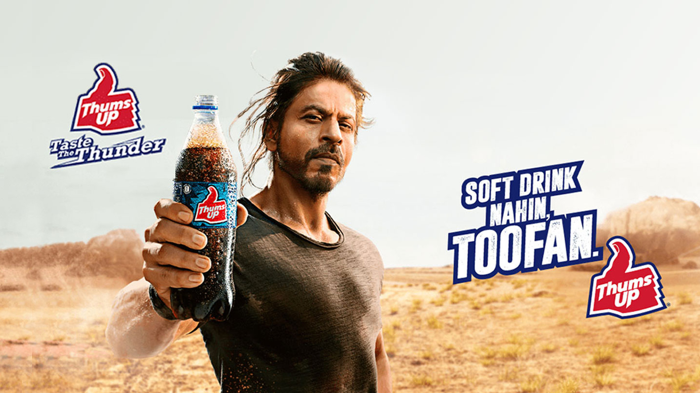 Thums up का बोतल पकड़ा हुआ व्यक्ति, जिसमें बोतल पर लिखा हुआ है: Soft drink makin Toofan