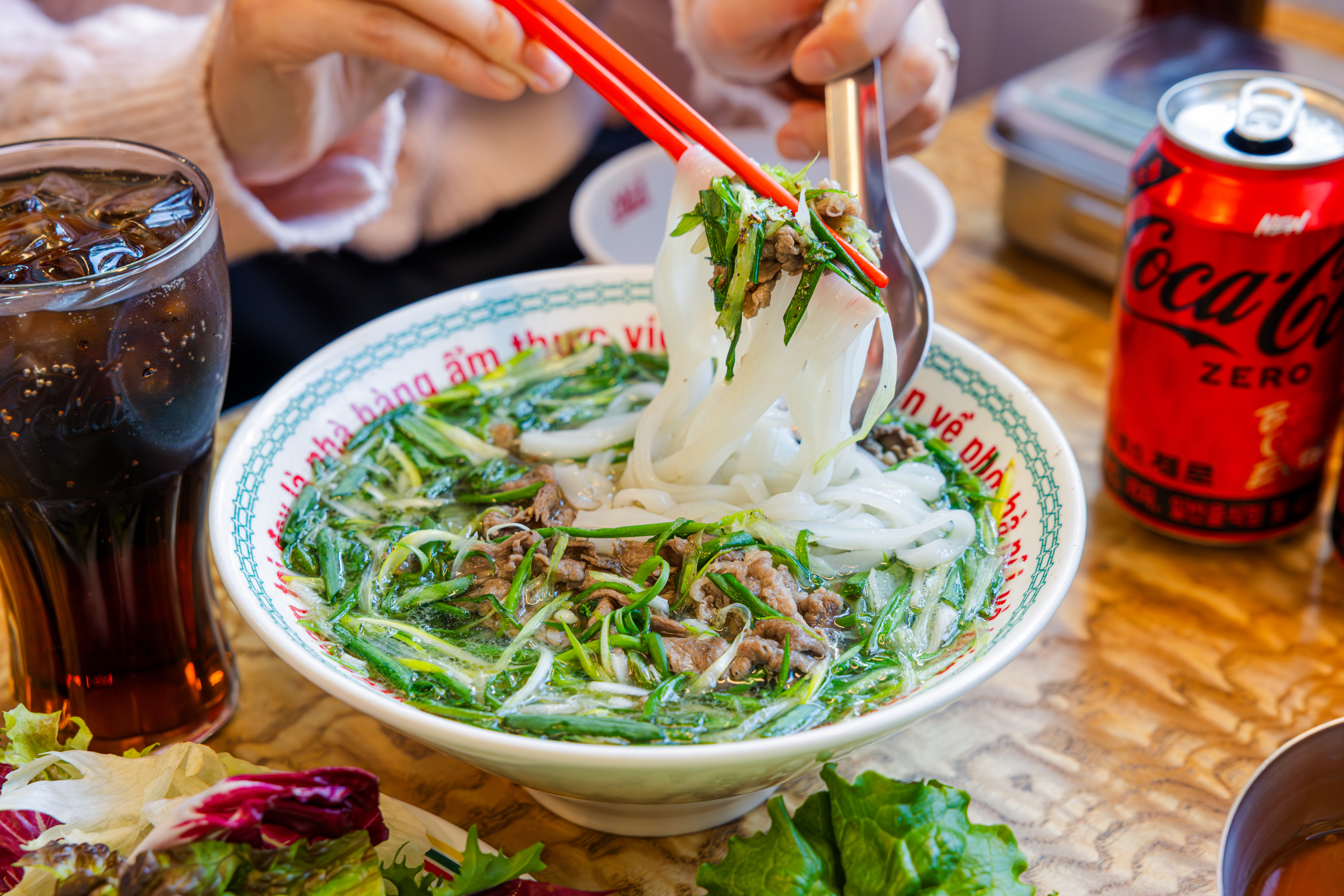 '꾸아 성수본점'의 대표메뉴, 한우사골직화칼국수를 코카-콜라 제로와 함께 즐기고 있다.v