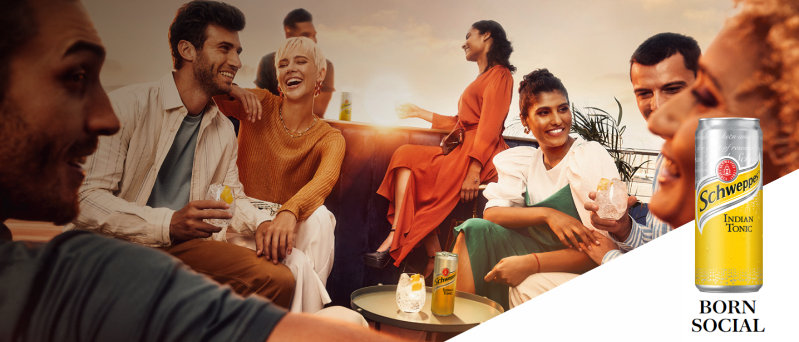 Oameni savurând băuturi Schweppes în aer liber la apus