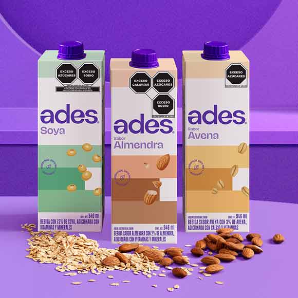 Tres cajas de bebidas Ades sobre un fondo púrpura. Sabores: Soya, Almendra y Avena. Ingredientes como avena y almendras están en primer plano.