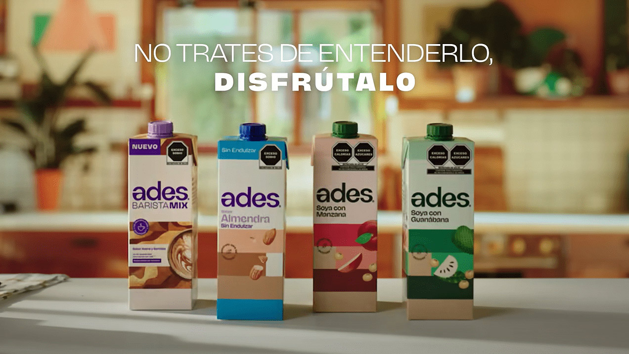  Cuatro cajas de bebidas vegetales Ades en una cocina acogedora. Los sabores incluyen Barista Mix, Almendra, Soya con Manzana y Soya con Guanábana. Texto destacado: 'No trates de entenderlo, disfrútalo'.