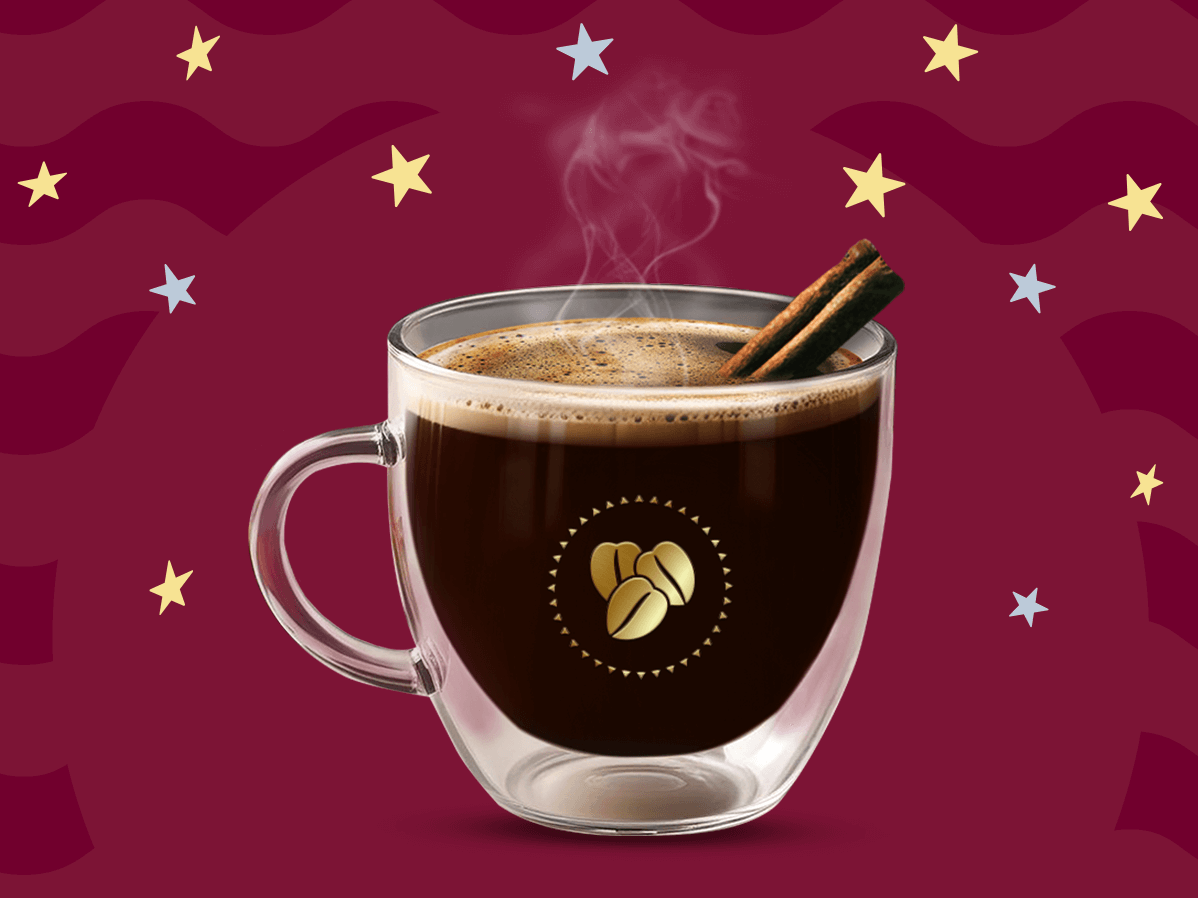 Una taza de cristal con café de olla caliente y dos varitas de canela sobre un fondo en tonos guinda.