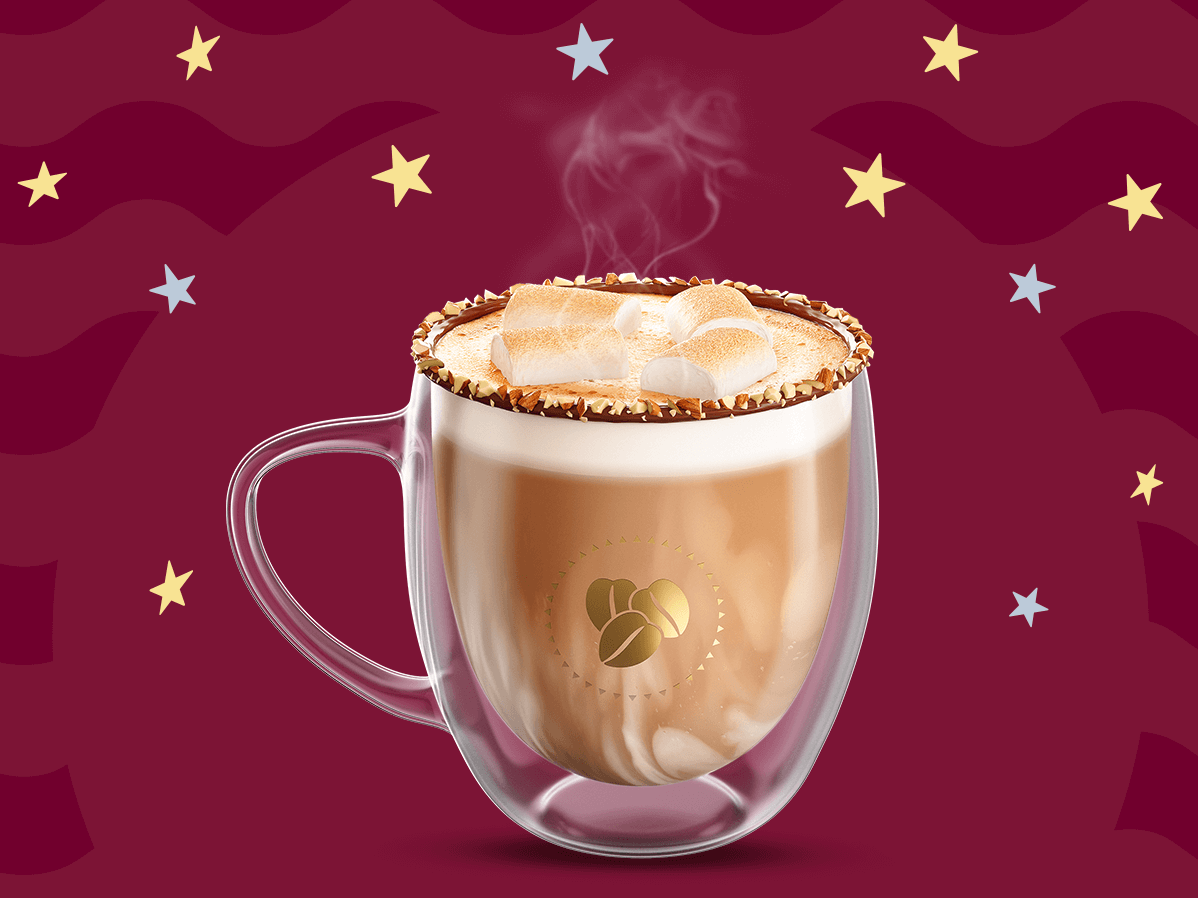 Una taza de cristal con café moka caliente y bombones rostizados por encima con nuez picada decorando los bordes de la taza sobre un fondo en tonos guinda.