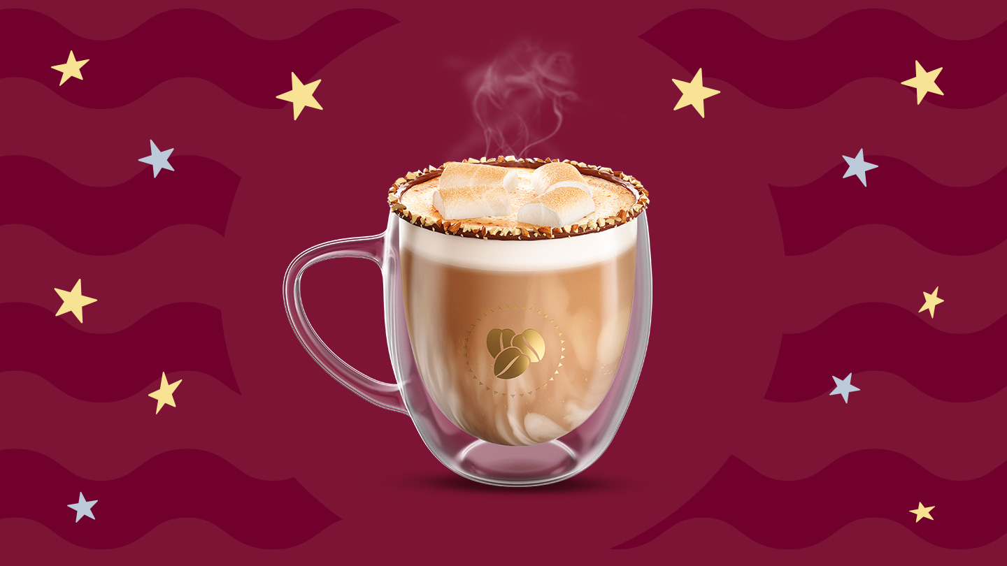 Una taza de cristal con café moka caliente y bombones rostizados por encima con nuez picada decorando los bordes de la taza sobre un fondo en tonos guinda.