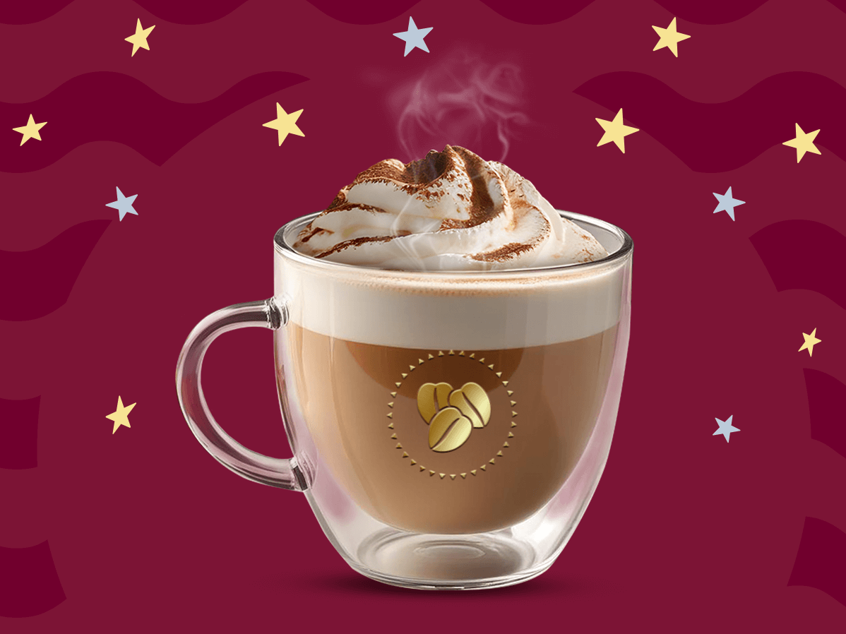 Una taza de cristal con cinnamon latte caliente y crema batida por encima decorado con canela en polvo por encima sobre un fondo en tonos guinda.