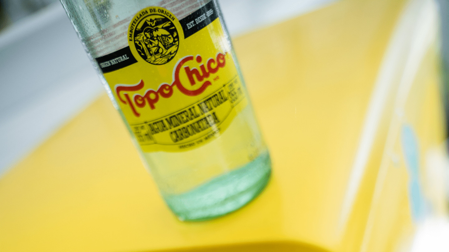 Botella de vidrio Topo Chico sobre una heladera amarillo Topo Chico