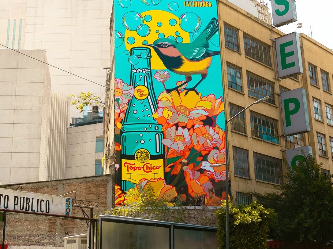 Edificio pintado con un hornero al lado de una botella Topo Chico.