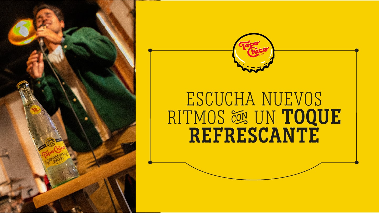 Un chico cantando con un botella de vidrio de Topo Chico delante sobre una mesa