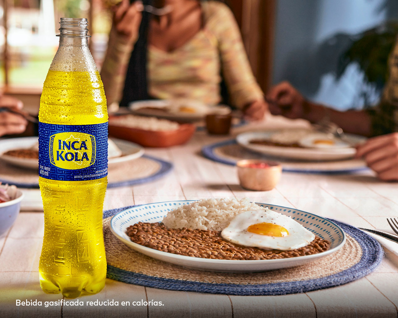 Una botella de Inca Kola sobre una mesa con 4 platos de comida.