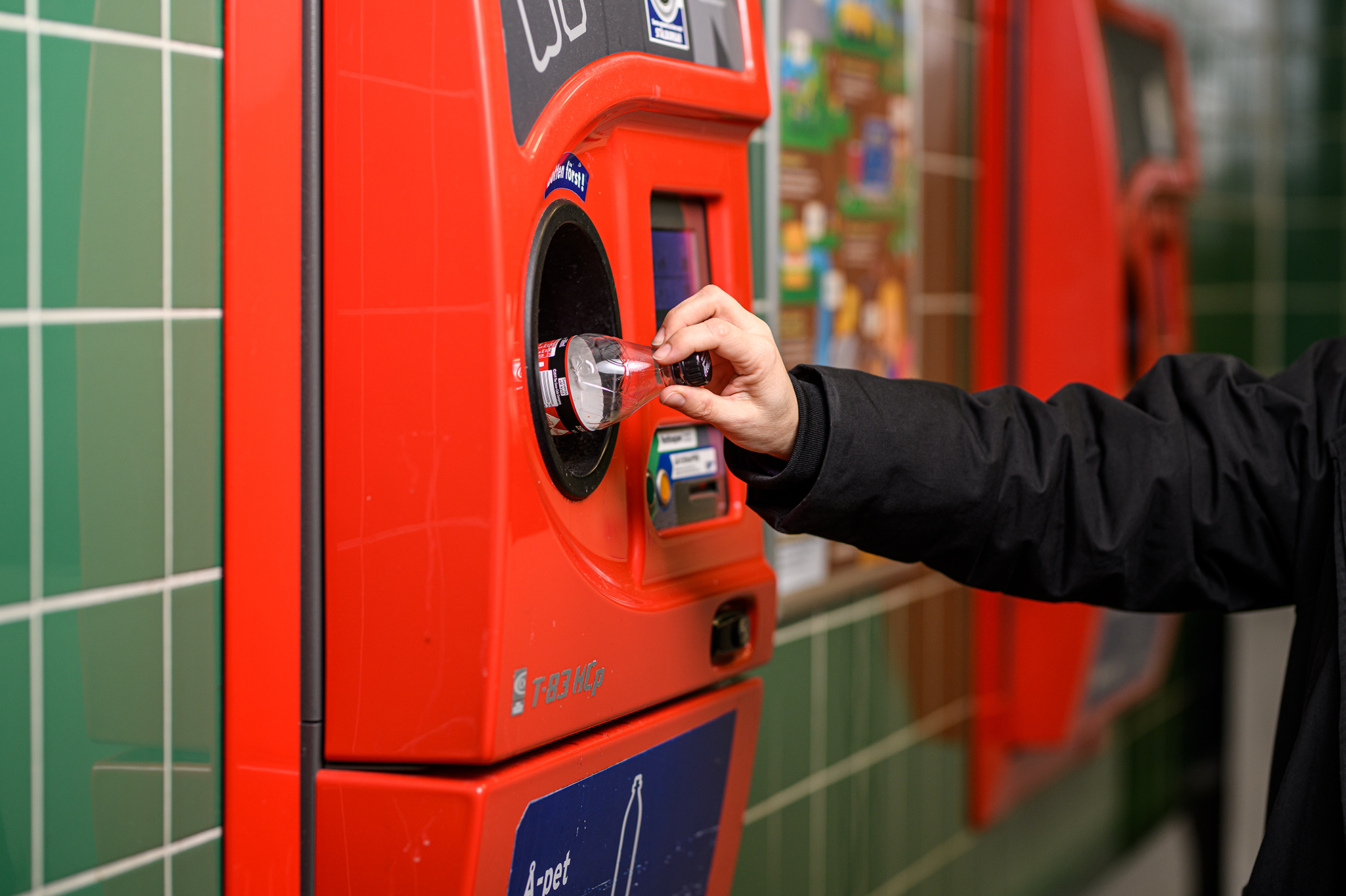 Hand som placerar en plastflaska i en röd returmaskin för återvinning.