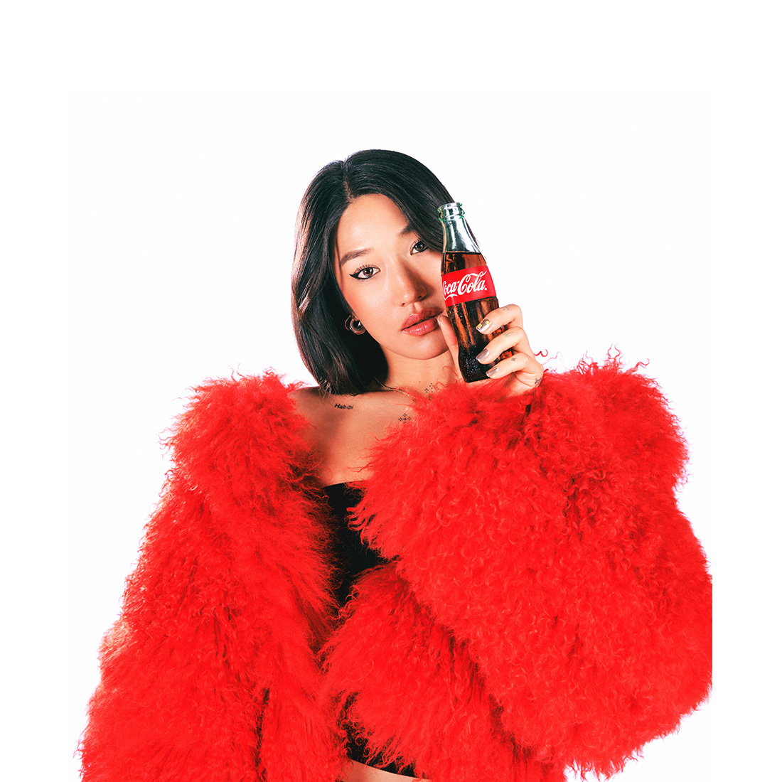 Peggy Gou posando con un llamativo abrigo de peluche rojo, pantalones brillantes y fondo blanco.