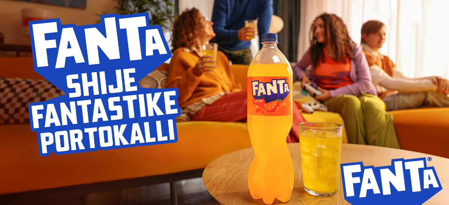 Familja është ulur në dhomën e ndenjës, luan video‑lojëra dhe shijon pijen, ndërsa shishja e Fantës me portokall është e theksuar në plan të parë si simbol i momenteve të përbashkëta dhe shijes së shkëlqyer.